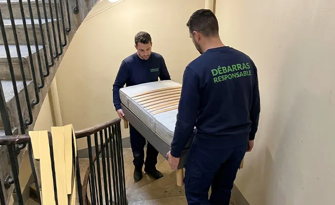 Deux professionnels Débarras Responsable descendant un sommier dans un escalier colimaçon étroit d'un immeuble ancien.