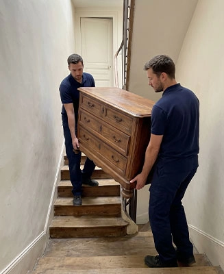 Équipe Débarras Responsable portant un meuble lourd dans l'escalier d'une maison de ville.