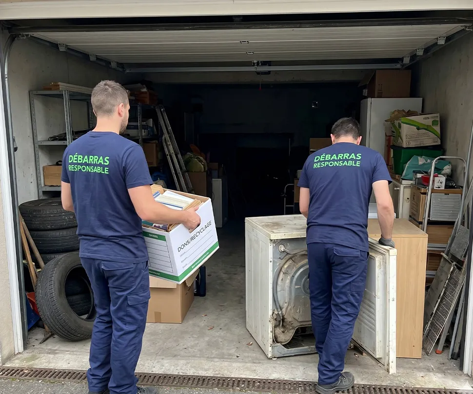 Deux professionnels de Débarras Responsable en uniforme bleu (texte vert) s'activent à l'entrée d'un garage souterrain encombré, gérant le tri et la manutention lourde.