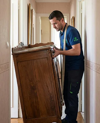 Professionnel de Débarras Responsable manœuvrant délicatement un buffet ancien en bois massif dans un couloir étroit lors du débarras d'une maison de succession.