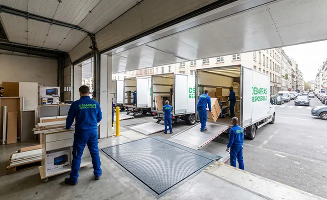 Perspective depuis l’intérieur d’un quai de chargement commercial vers la rue où plusieurs camions Débarras Responsable sont en cours de chargement.
